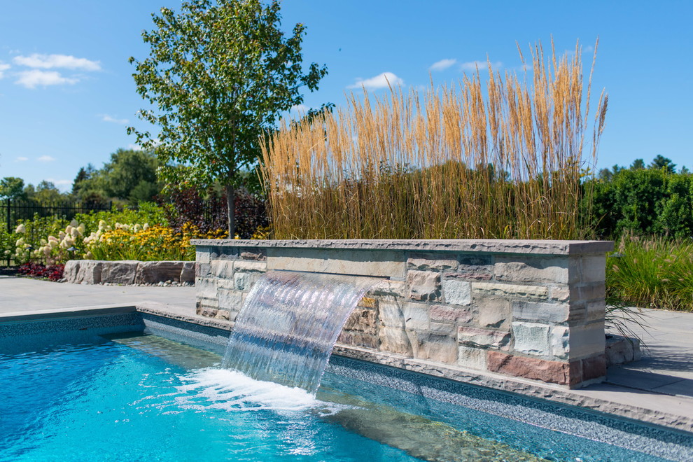 Photo of a large contemporary back rectangular lengths swimming pool with a water feature and brick paving.