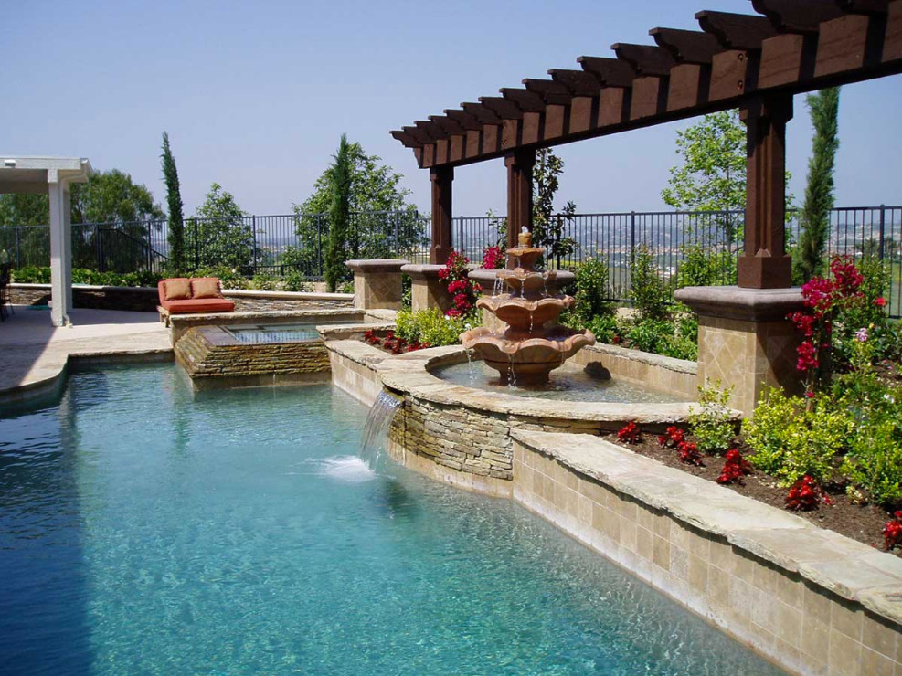 Design ideas for a large mediterranean back custom shaped natural swimming pool in Orange County with a water feature and stamped concrete.