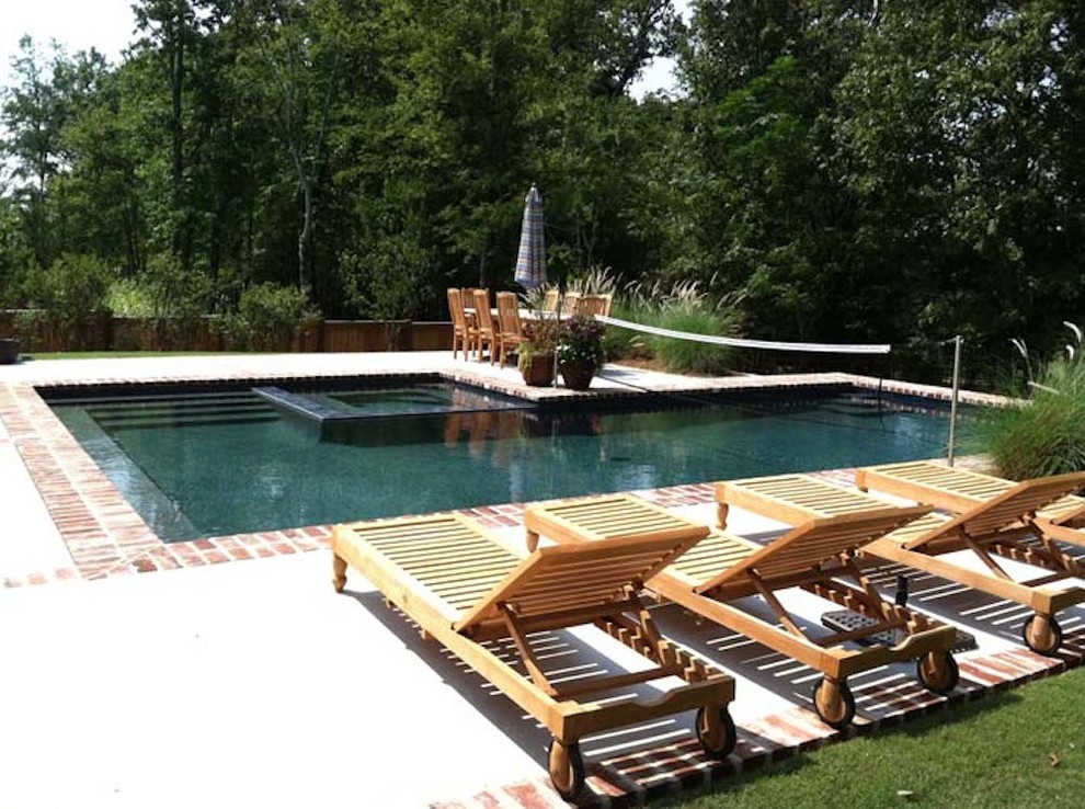 Modelo de piscina con fuente alargada tradicional grande a medida en patio trasero con adoquines de ladrillo