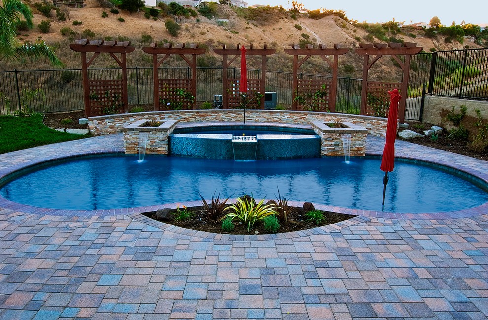 Modelo de piscinas y jacuzzis naturales mediterráneos de tamaño medio tipo riñón en patio trasero con adoquines de hormigón