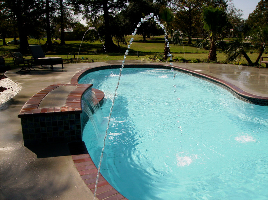 Esempio di una grande piscina tradizionale personalizzata dietro casa con una vasca idromassaggio e lastre di cemento