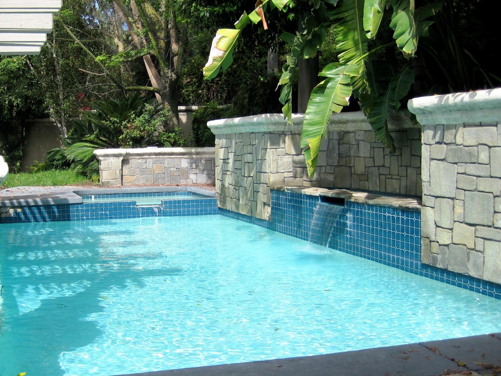 Immagine di una piscina tropicale rettangolare di medie dimensioni e dietro casa con fontane e pavimentazioni in cemento