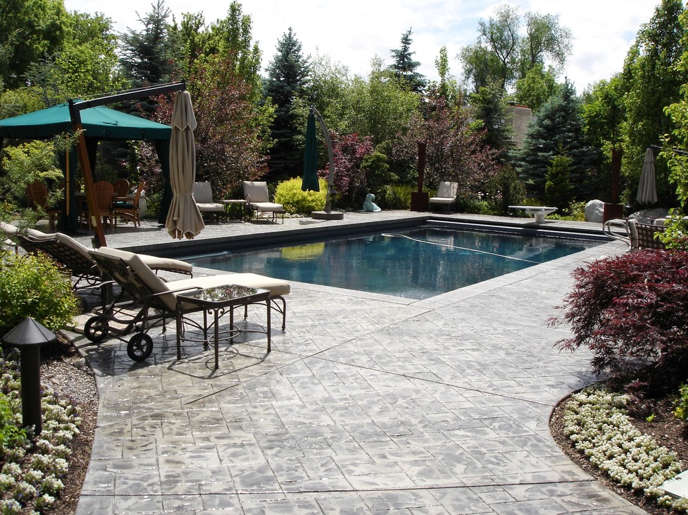 На фото: большой прямоугольный ландшафтный бассейн на заднем дворе в классическом стиле с покрытием из декоративного бетона с