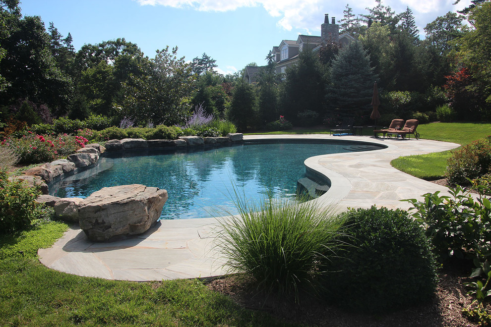 Modelo de piscina elevada tradicional renovada grande tipo riñón en patio trasero con adoquines de piedra natural