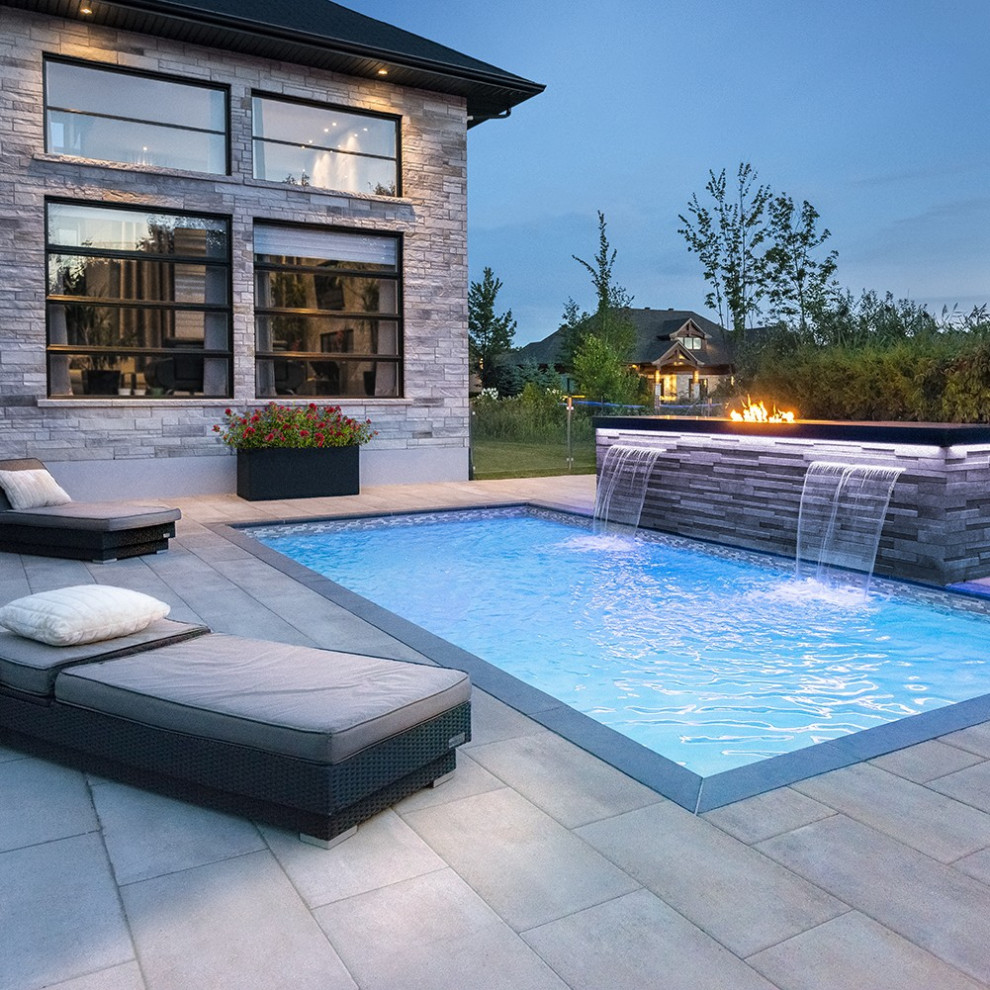 Ejemplo de piscina con fuente actual de tamaño medio rectangular en patio trasero con suelo de baldosas