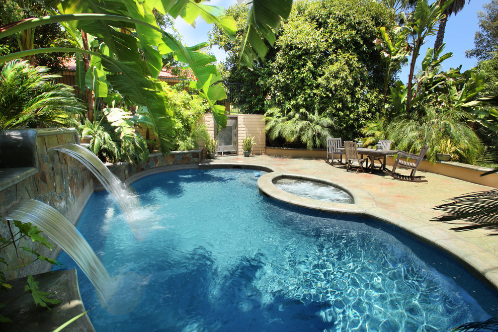 Modelo de piscinas y jacuzzis tradicionales tipo riñón en patio lateral con suelo de hormigón estampado