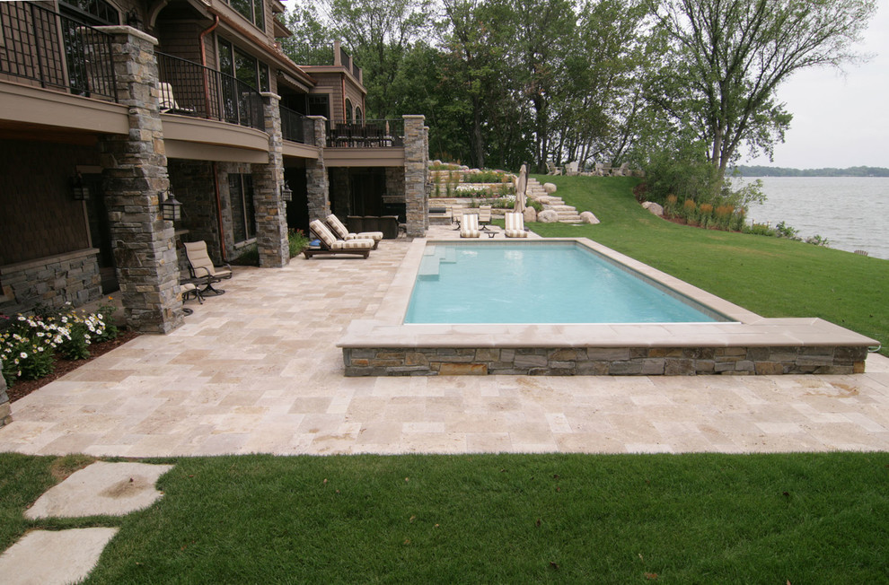 Diseño de piscina elevada clásica extra grande rectangular en patio trasero con adoquines de piedra natural