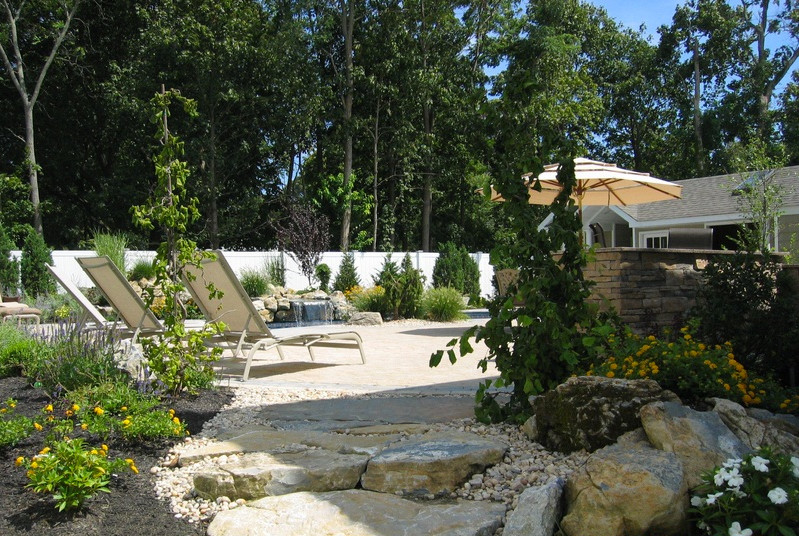 Diseño de piscina con fuente natural minimalista redondeada en patio trasero con adoquines de piedra natural