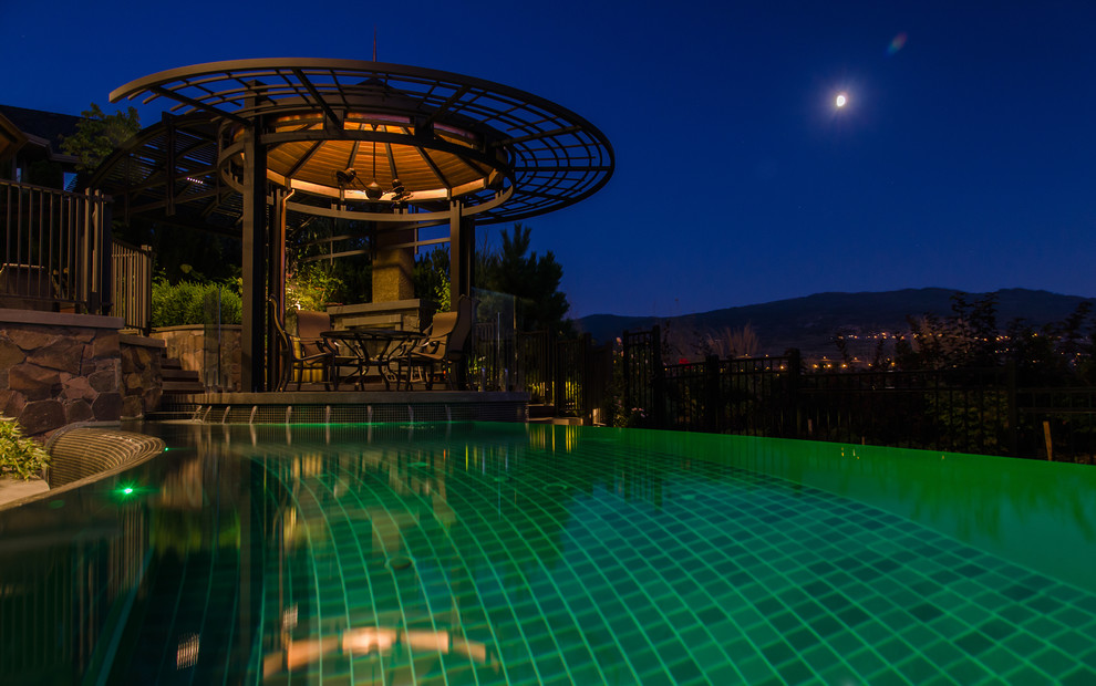 Foto di una piscina a sfioro infinito design personalizzata di medie dimensioni e dietro casa con pavimentazioni in pietra naturale