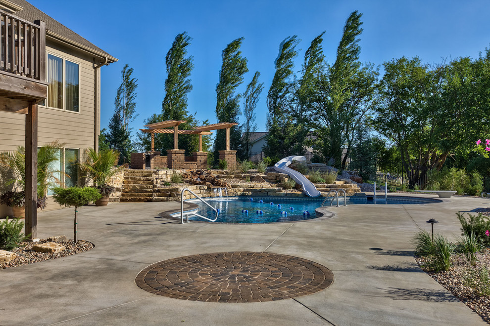 Imagen de piscina con tobogán rústica grande a medida en patio trasero con adoquines de hormigón