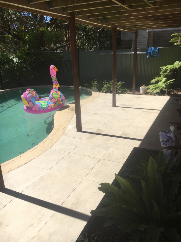 Bild på en mellanstor funkis njurformad pool på baksidan av huset, med kakelplattor