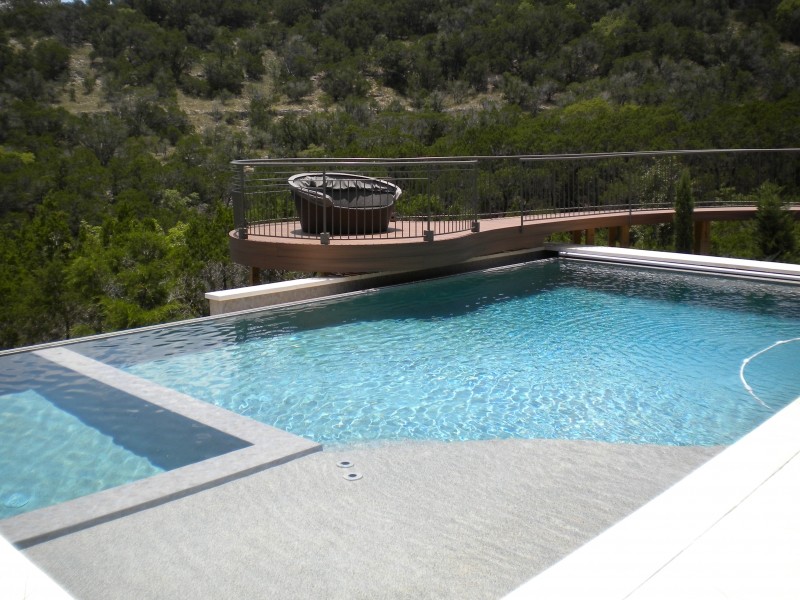 Aménagement d'une grande piscine à débordement et arrière contemporaine rectangle avec un bain bouillonnant et des pavés en pierre naturelle.