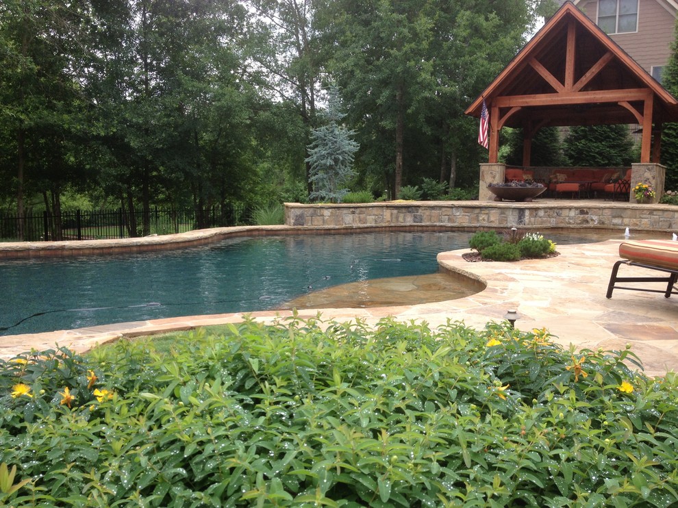 Esempio di un'ampia piscina naturale tradizionale personalizzata dietro casa con fontane e pavimentazioni in pietra naturale