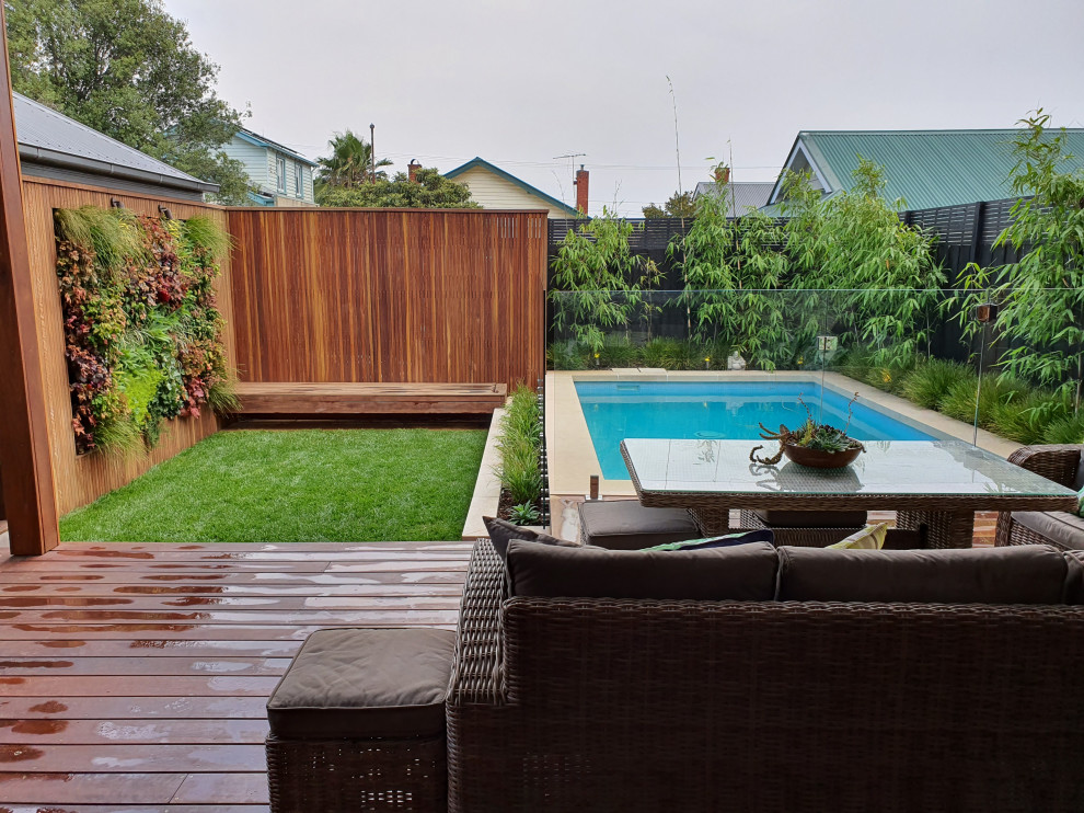 Exemple d'un grand piscine avec aménagement paysager arrière moderne rectangle avec une terrasse en bois.