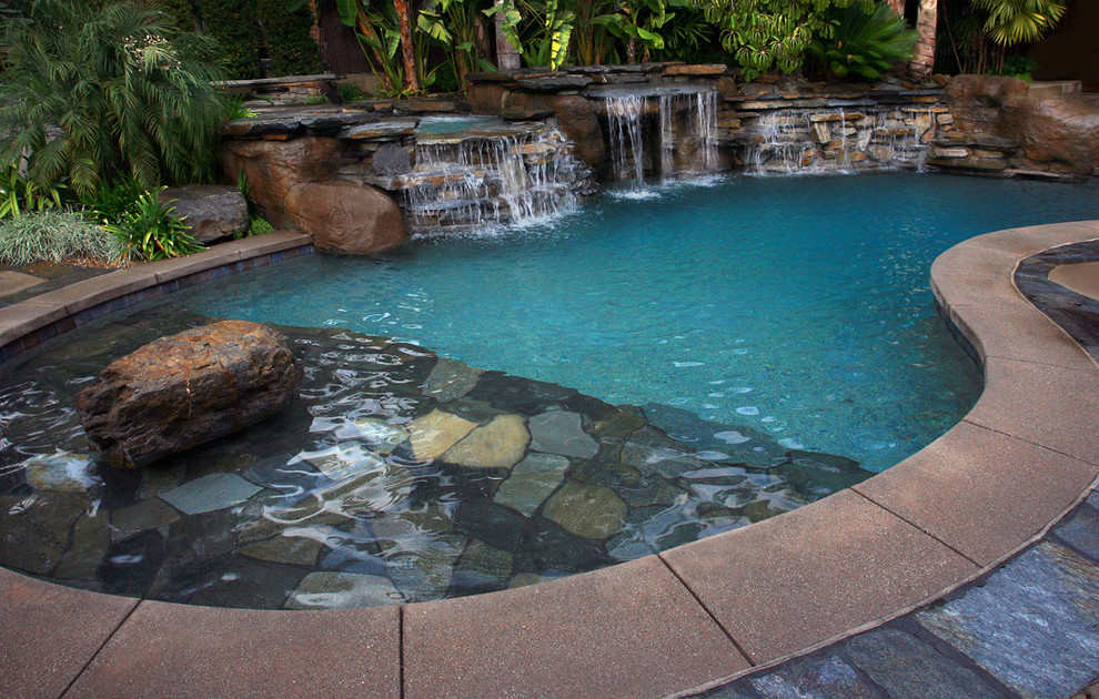 This is an example of a large world-inspired back kidney-shaped lengths swimming pool in Los Angeles with a water feature and natural stone paving.