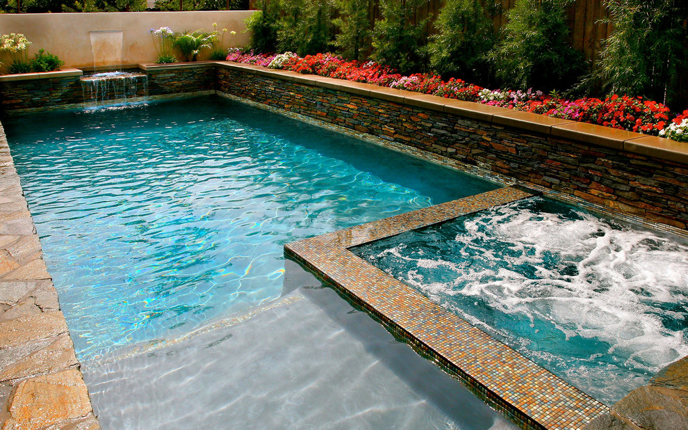 Imagen de piscina con fuente alargada tropical de tamaño medio rectangular en patio trasero con adoquines de piedra natural