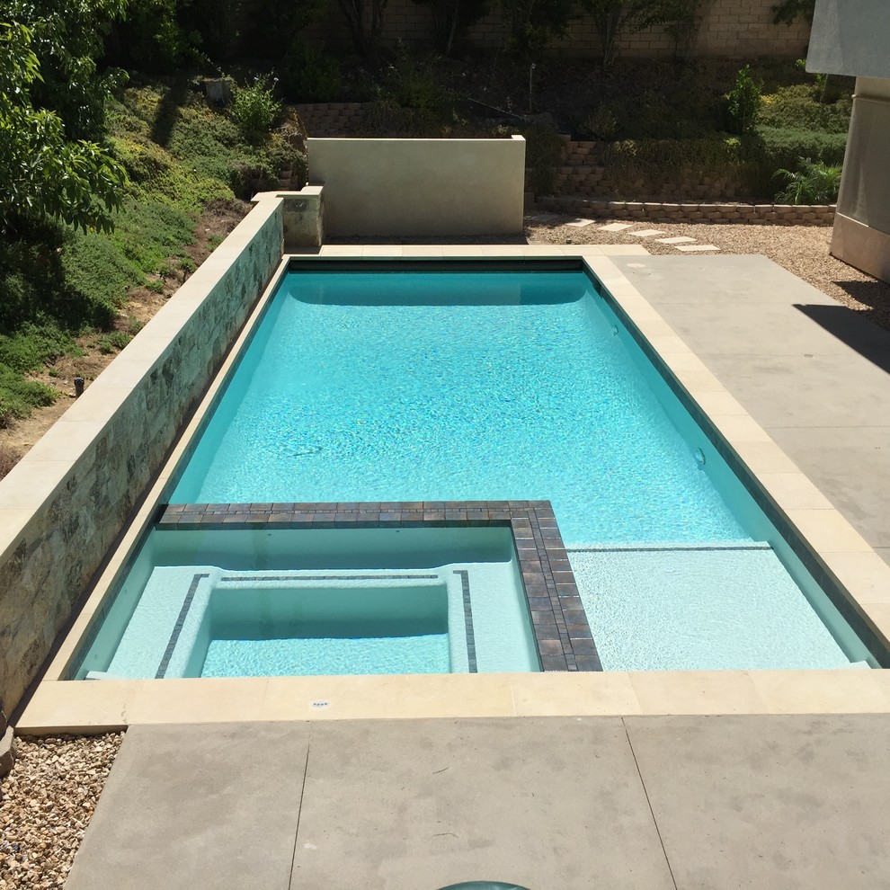 Modelo de piscina mediterránea rectangular en patio trasero con losas de hormigón