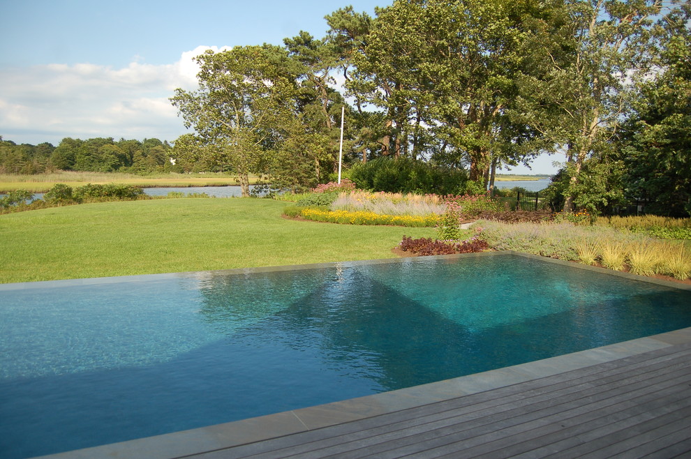 Пример оригинального дизайна: прямоугольный бассейн-инфинити среднего размера на заднем дворе в стиле неоклассика (современная классика) с настилом