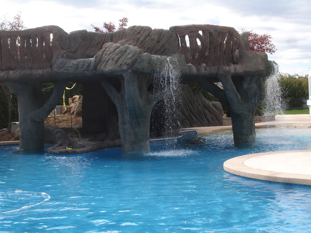 Ejemplo de piscina con fuente natural tropical grande a medida en patio trasero