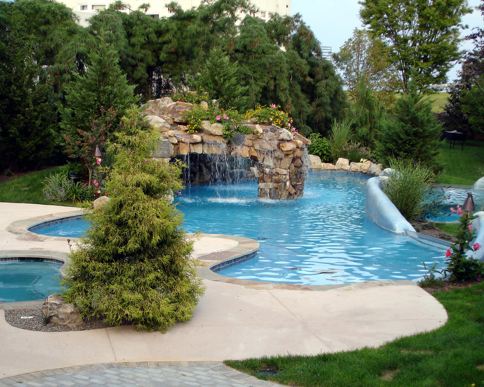 Immagine di una grande piscina monocorsia tropicale personalizzata dietro casa con fontane e lastre di cemento