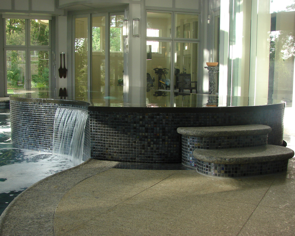 Inspiration pour une grande piscine intérieure à débordement design en forme de haricot avec un bain bouillonnant et des pavés en pierre naturelle.