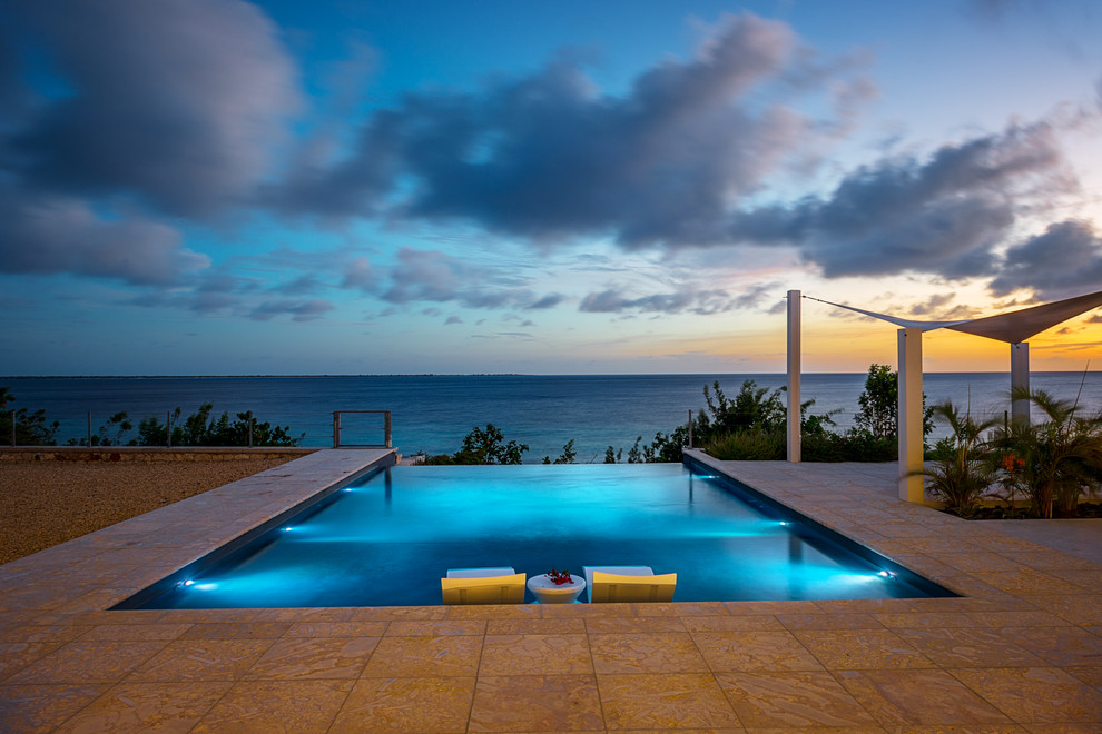 Ejemplo de piscina infinita minimalista grande rectangular en patio trasero con adoquines de piedra natural