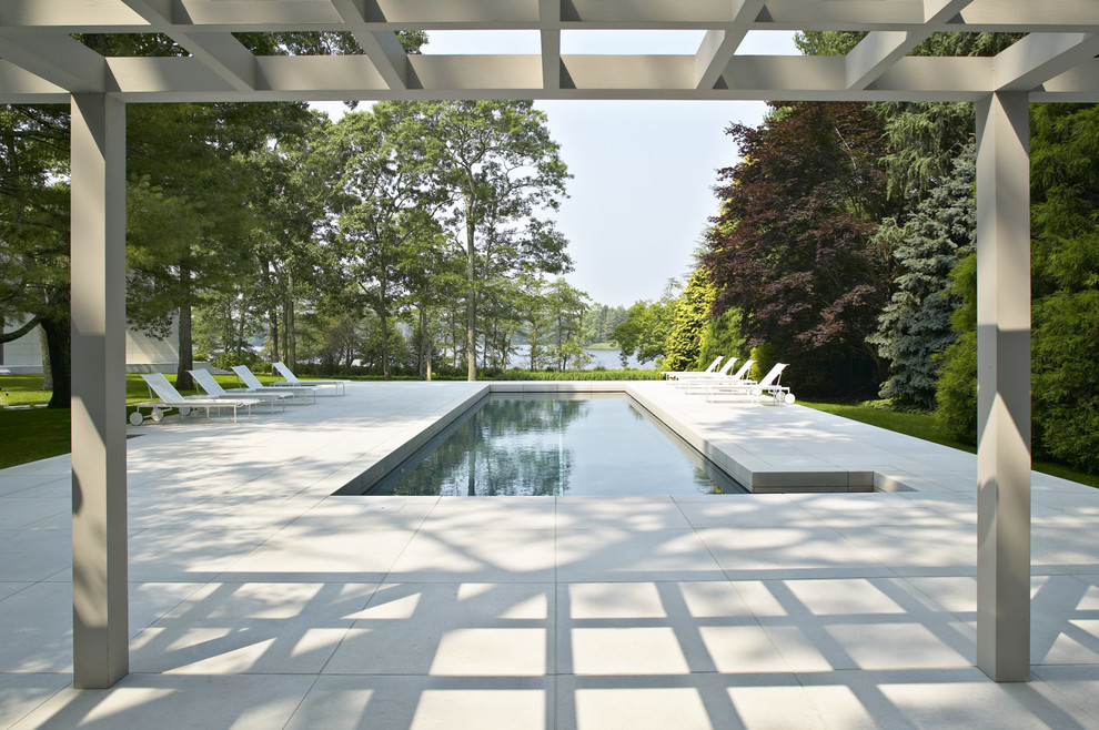 Modelo de piscina alargada moderna rectangular en patio trasero con adoquines de hormigón