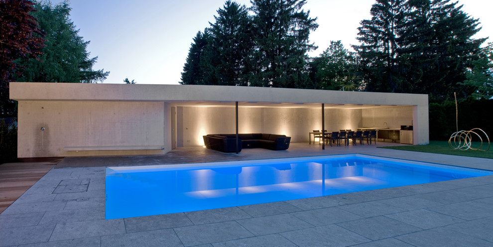 Imagen de casa de la piscina y piscina alargada contemporánea grande rectangular en patio trasero con losas de hormigón