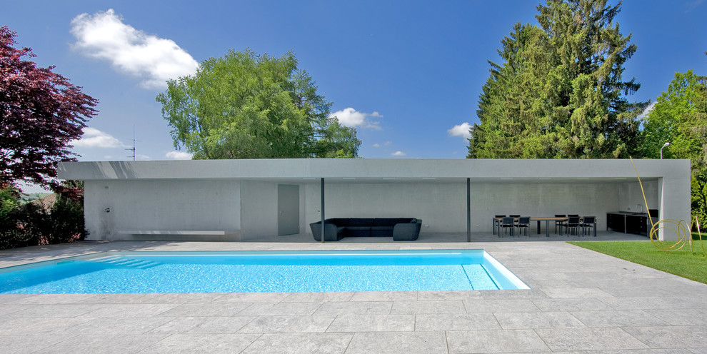 Foto de casa de la piscina y piscina alargada actual de tamaño medio rectangular en patio trasero con losas de hormigón
