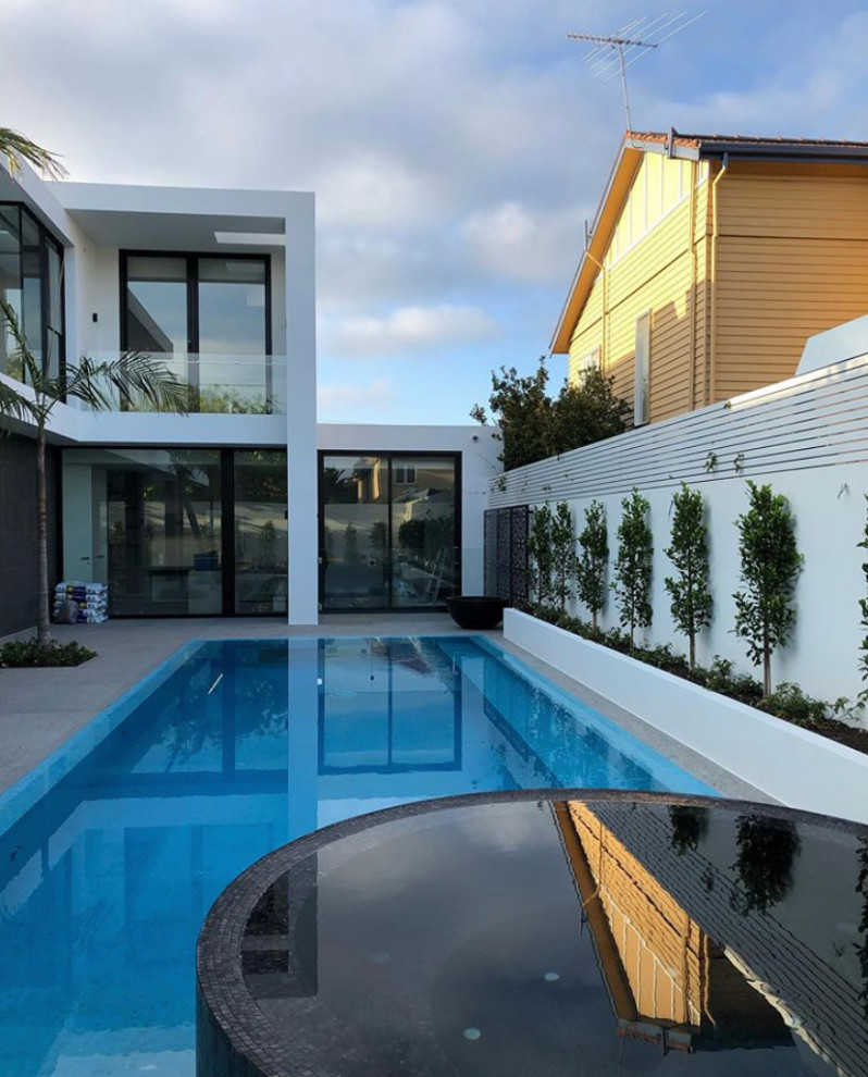 Diseño de piscina alargada minimalista grande rectangular en patio trasero con paisajismo de piscina y adoquines de hormigón