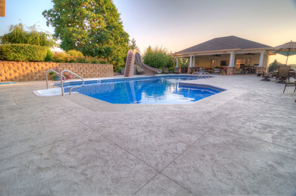 Inspiration for a large classic back custom shaped natural swimming pool in Cedar Rapids with a water slide and stamped concrete.
