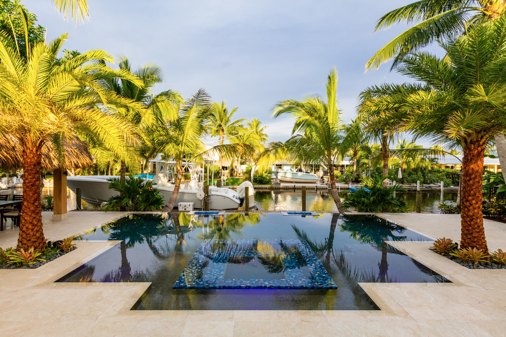 Diseño de piscinas y jacuzzis infinitos tropicales de tamaño medio rectangulares en patio trasero con adoquines de piedra natural