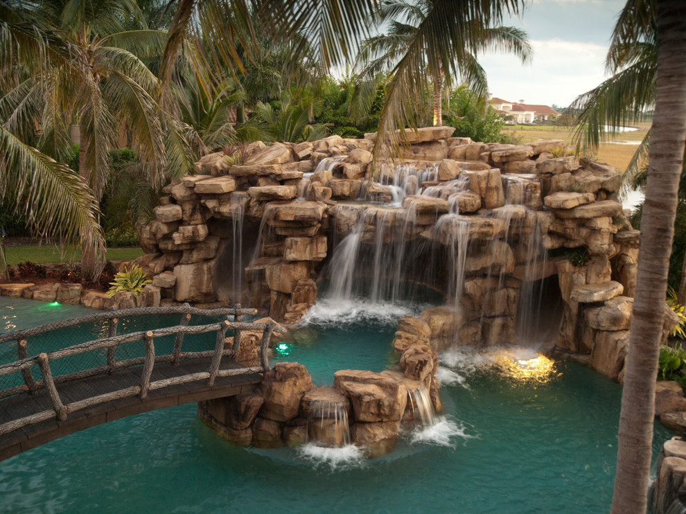 Immagine di una grande piscina monocorsia tropicale personalizzata dietro casa con pavimentazioni in pietra naturale e una vasca idromassaggio