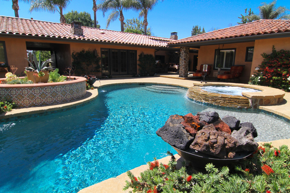 Bild på en mellanstor medelhavsstil njurformad pool på baksidan av huset, med naturstensplattor och spabad