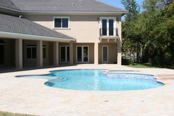 Example of a classic backyard brick and custom-shaped hot tub design in Miami