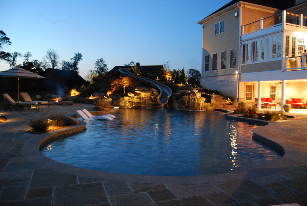 Esempio di un'ampia piscina naturale chic personalizzata dietro casa con un acquascivolo e pavimentazioni in pietra naturale