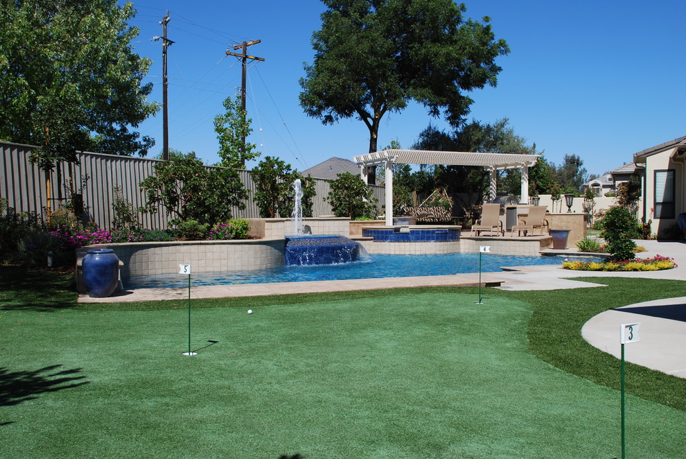 Ejemplo de piscina con fuente actual grande a medida en patio trasero con losas de hormigón