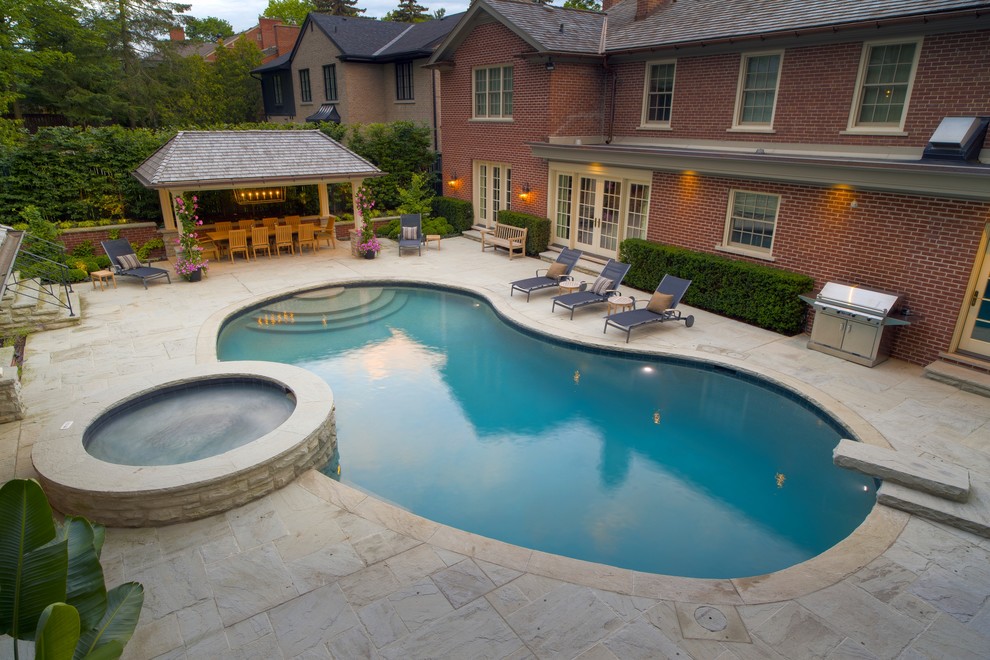 Пример оригинального дизайна: бассейн среднего размера, в форме фасоли на заднем дворе в классическом стиле с джакузи и покрытием из каменной брусчатки