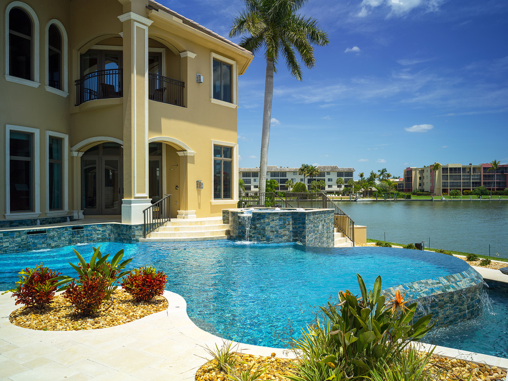 Bild på en tropisk anpassad infinitypool på baksidan av huset, med en fontän och naturstensplattor