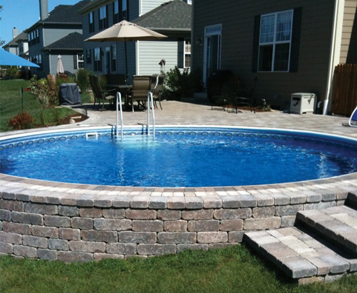 Ejemplo de piscina elevada clásica de tamaño medio a medida en patio trasero con adoquines de ladrillo
