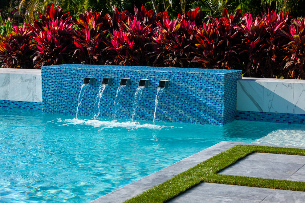 Diseño de piscina con fuente moderna grande a medida en patio trasero con adoquines de piedra natural