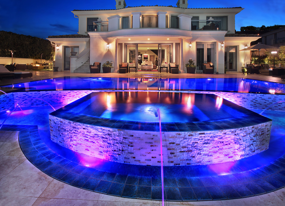 Imagen de piscina con fuente infinita actual grande a medida en patio trasero con adoquines de piedra natural