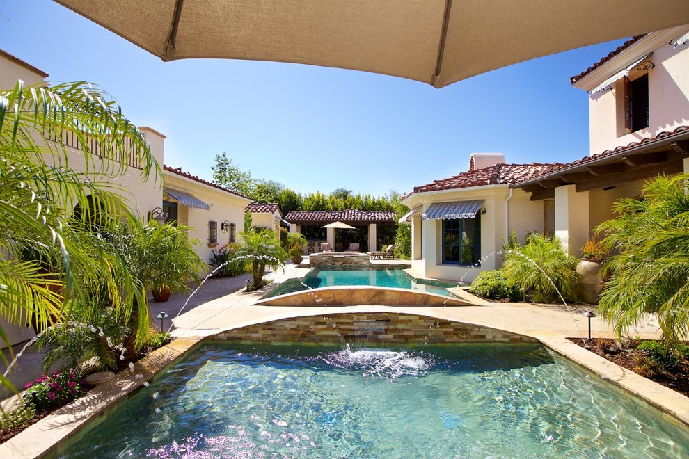 This is an example of an expansive mediterranean courtyard rectangular natural swimming pool in San Diego with a pool house and natural stone paving.