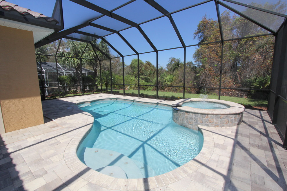 Cette image montre une grande piscine naturelle et arrière traditionnelle en forme de haricot avec un bain bouillonnant et des pavés en béton.