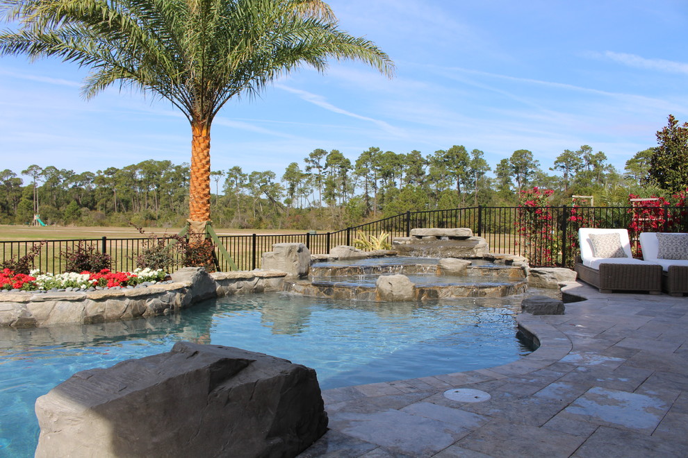 Ejemplo de piscina con fuente tropical a medida en patio trasero con adoquines de piedra natural