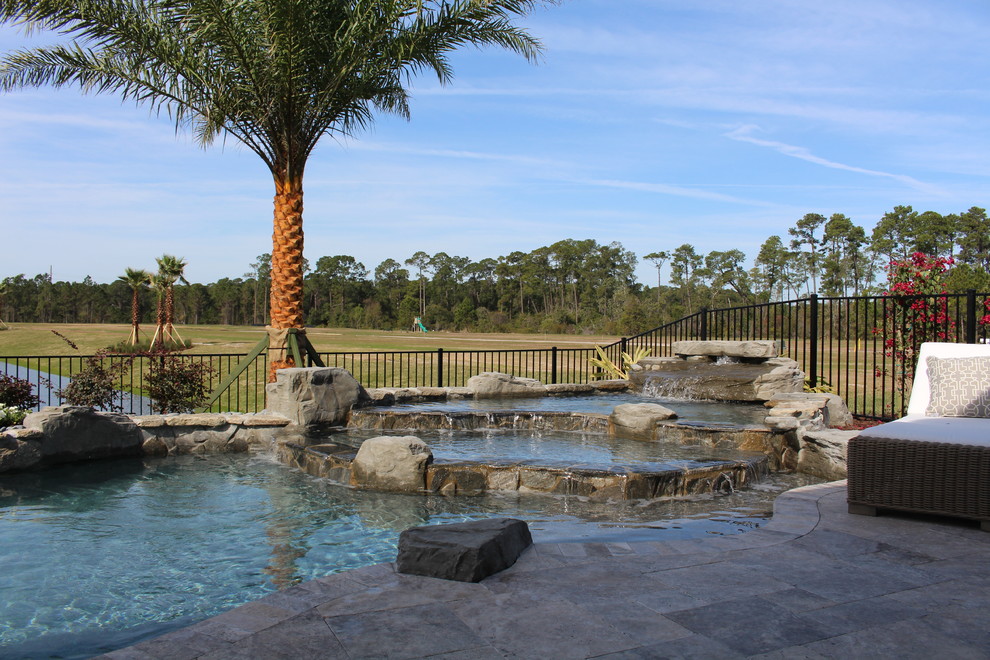 Modelo de piscina con fuente tropical a medida en patio trasero con adoquines de piedra natural