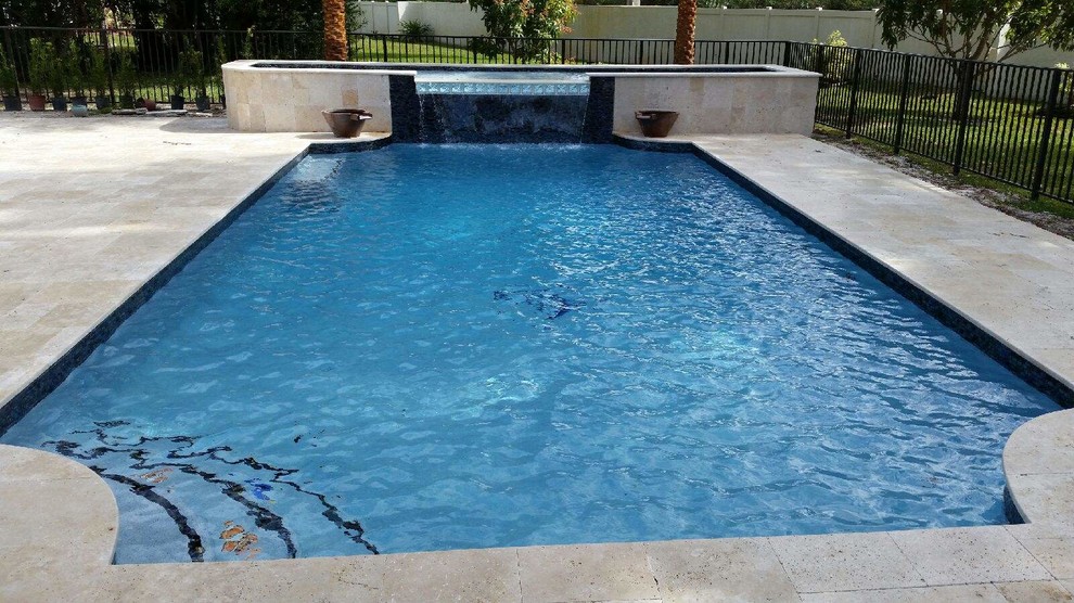 This is an example of a medium sized modern back custom shaped lengths swimming pool in Miami with a water feature and natural stone paving.