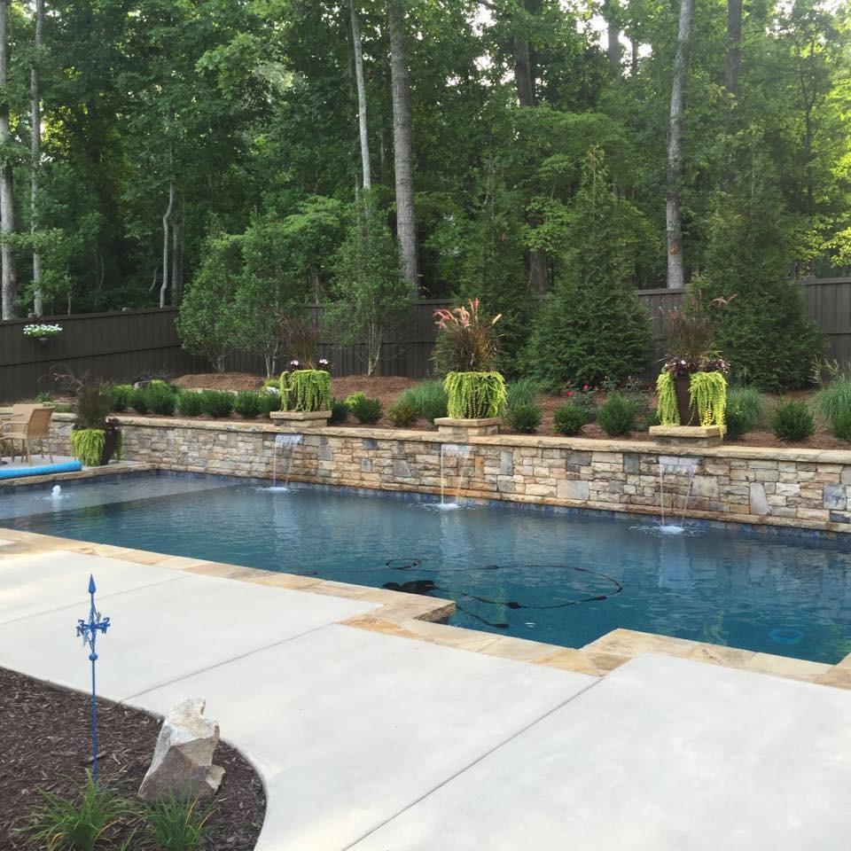 Aménagement d'une grande piscine arrière classique rectangle avec un point d'eau et une dalle de béton.
