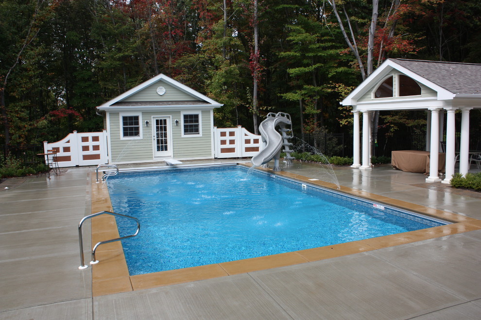 Medium sized traditional back rectangular lengths swimming pool in Other with a pool house and concrete slabs.