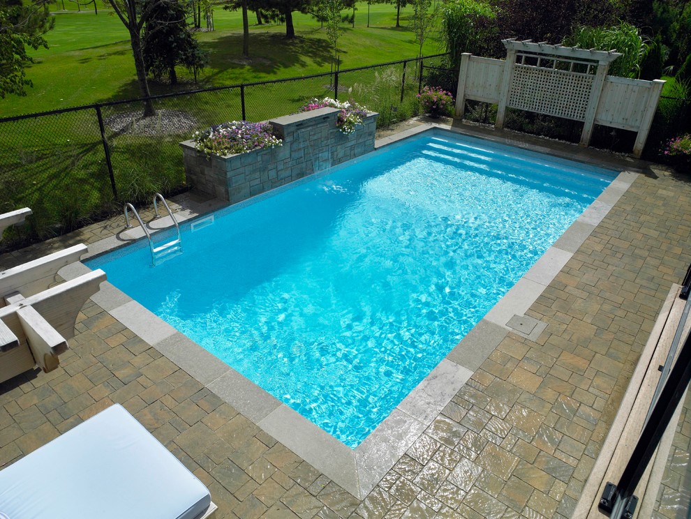 Photo of a large modern back rectangular natural swimming pool in Toronto with a water feature and brick paving.